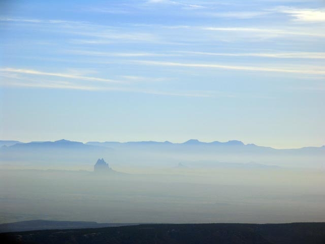 Distant view of a hazy desert landscape with rock formations under a blue sky.