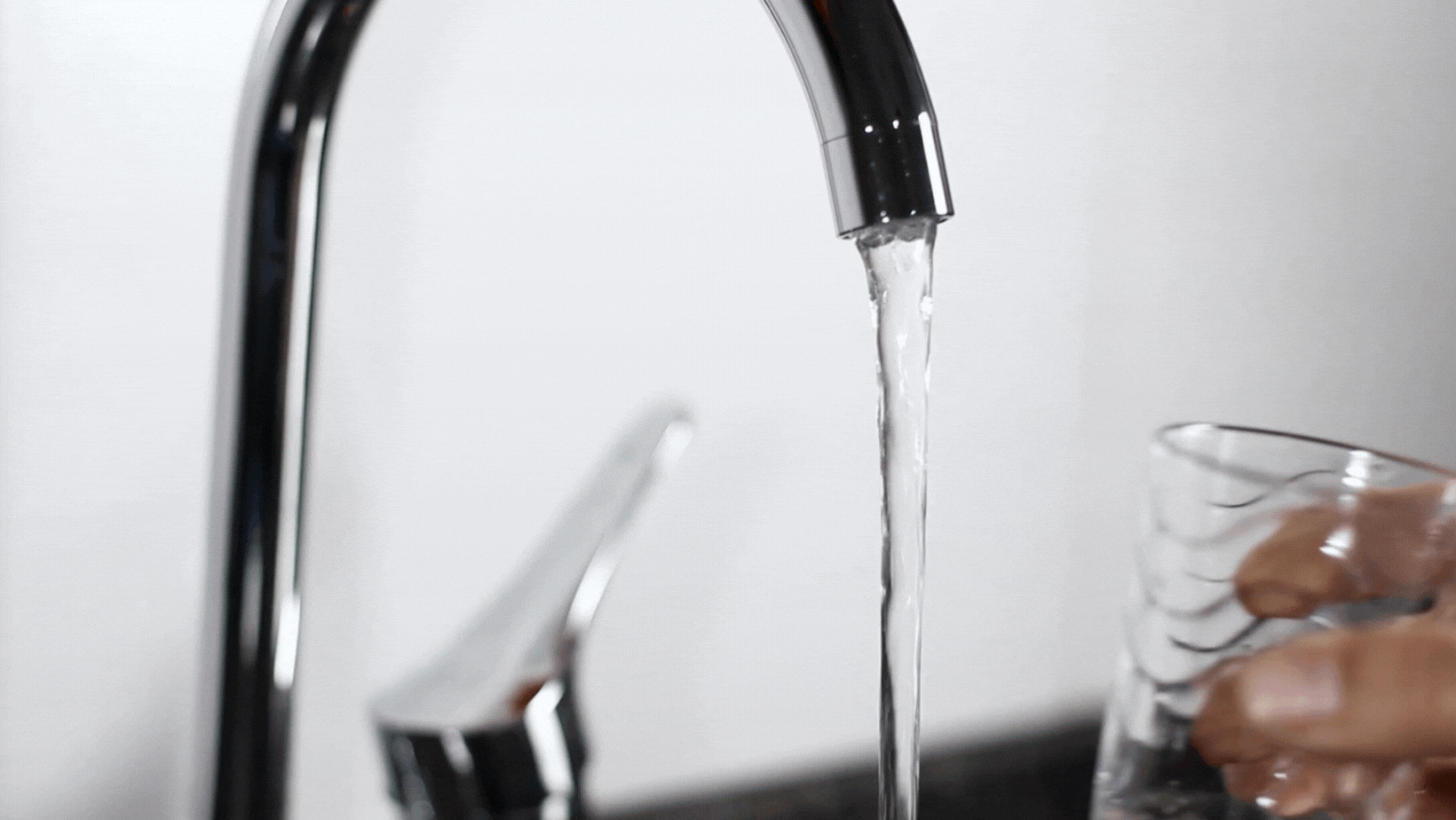 Person filling a glass of water from a kitchen tap