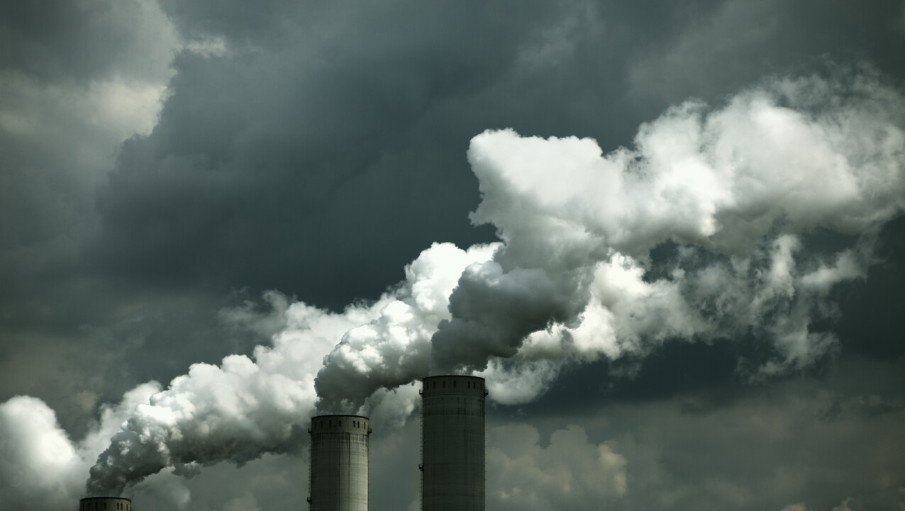 Three industrial coal smokestacks emit thick white smoke against a cloudy sky.