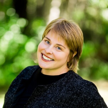 A person smiling outdoors with a blurred green background.