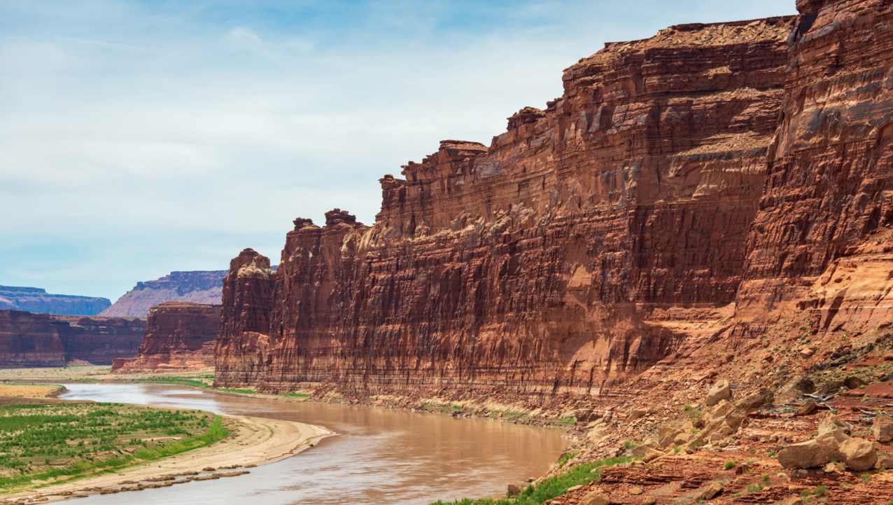 Red rock canyon with a river winding through green vegetation under a blue sky.