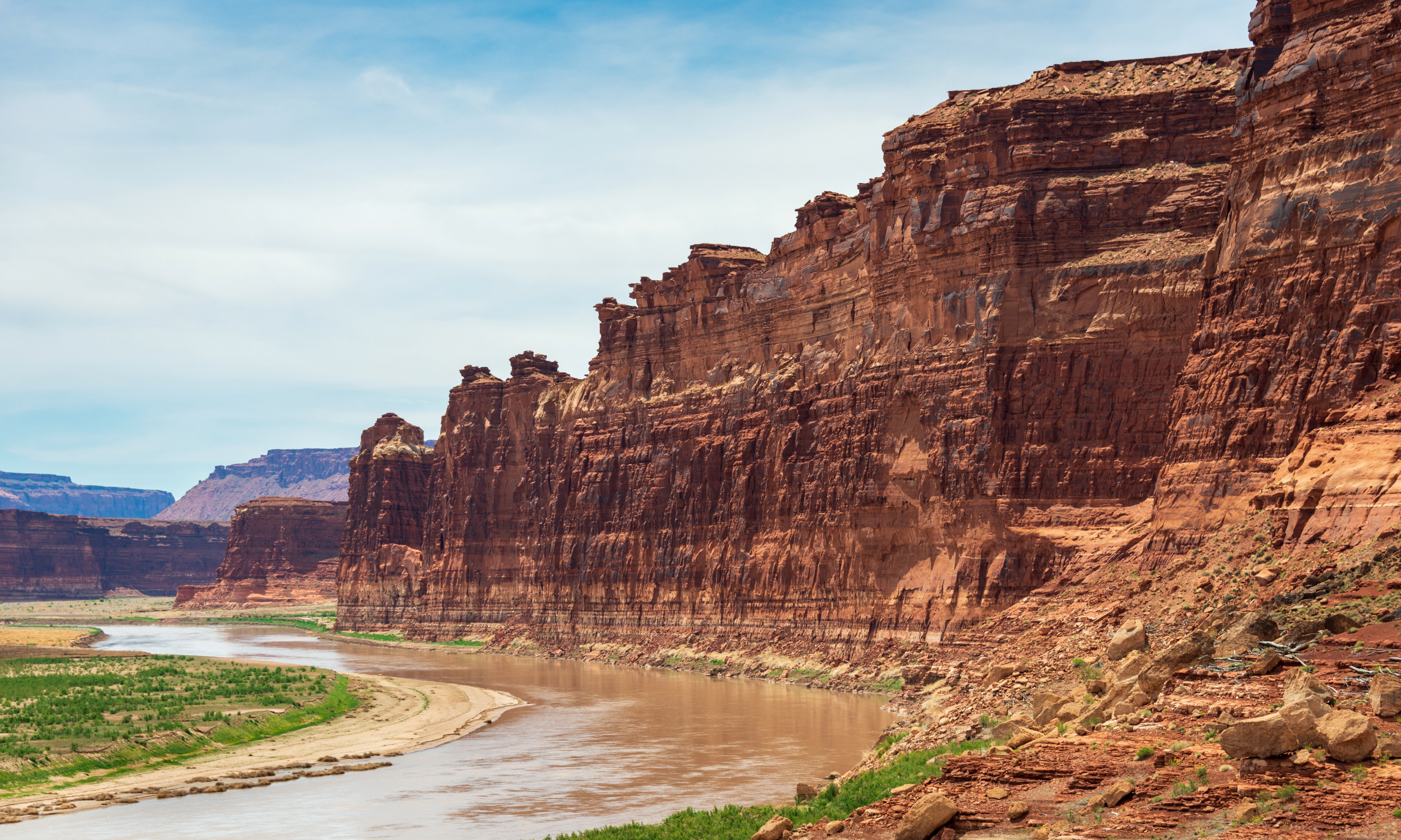 Red rock canyon with a river winding through green vegetation under a blue sky.