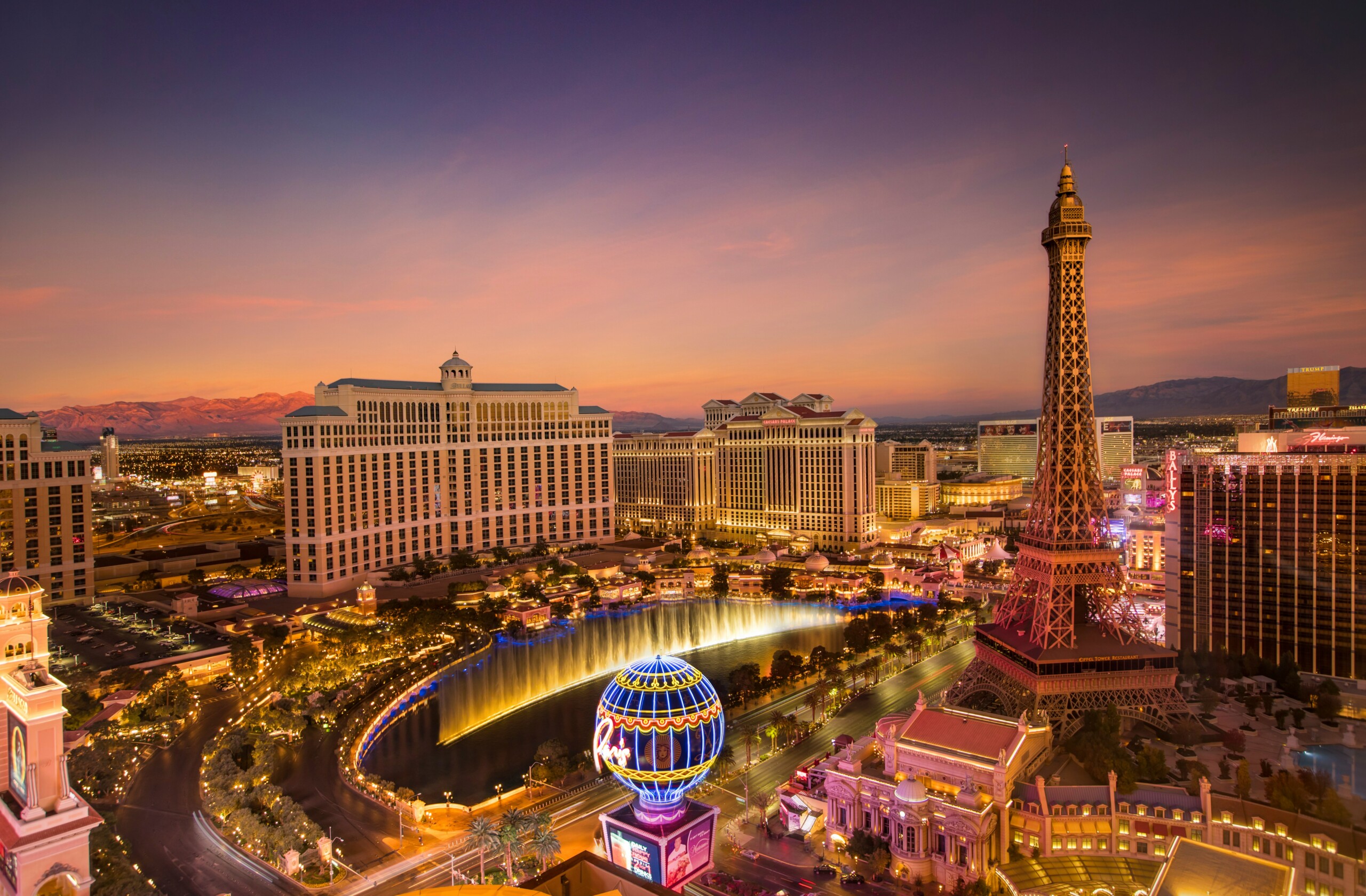 Aerial view of Las Vegas Strip at sunset, featuring iconic hotels, fountains, and the replica Eiffel Tower.