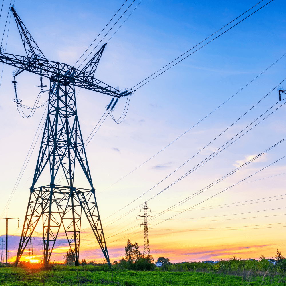 power lines High-voltage power lines and transmission towers stand in a green field at sunset under a partly cloudy sky.