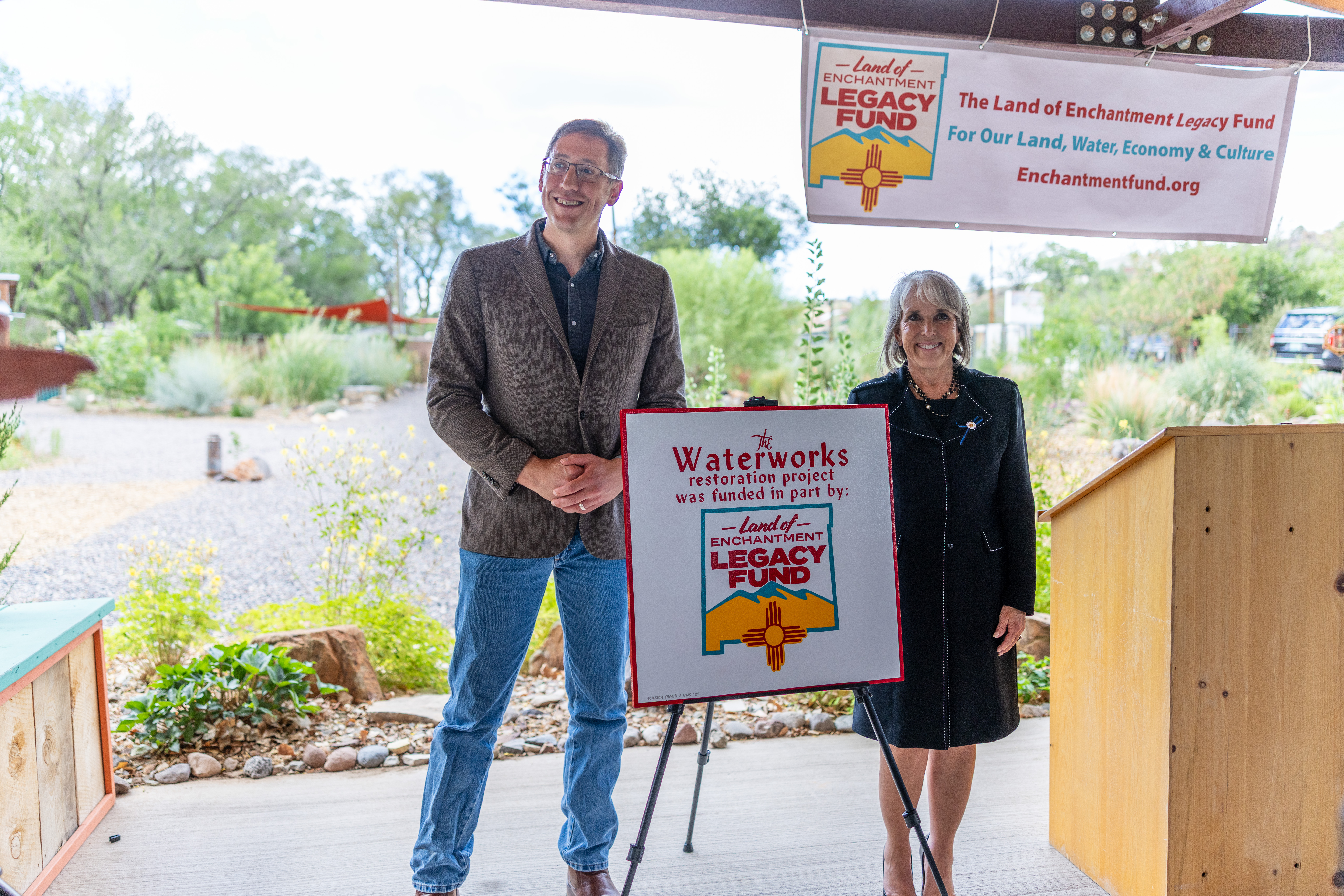 Governor Lujan Grisham and Representative Nathan Small smile together after unveiling a sign that reads 'Waterworks restoration project was funded in part by the Land of Enchantment Legacy Fund.'