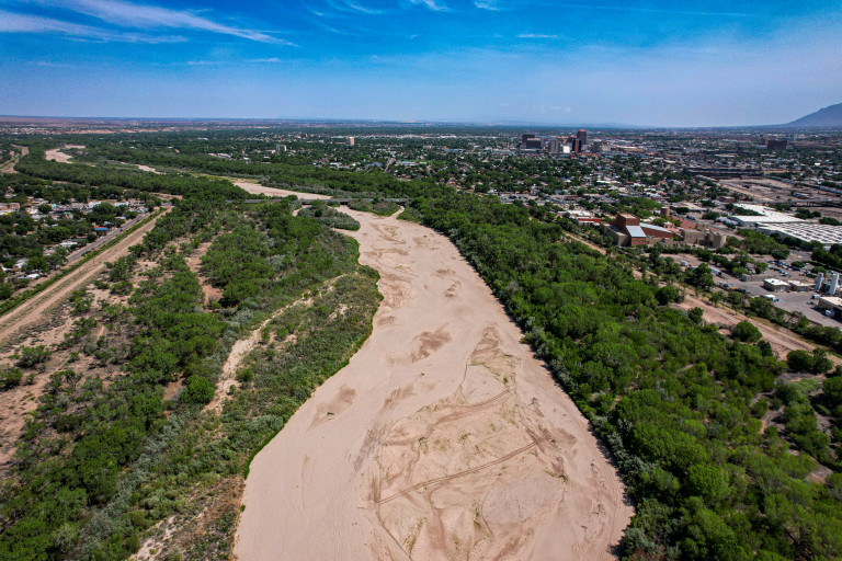 A dry stretch of the Rio Grande with the Albuquerque skyline in the background.
